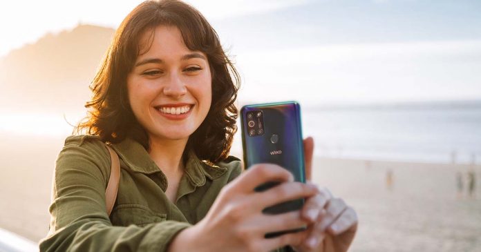 Beautiful woman taking selfie with her phone on the beach criar conteúdos nas férias com Wiko