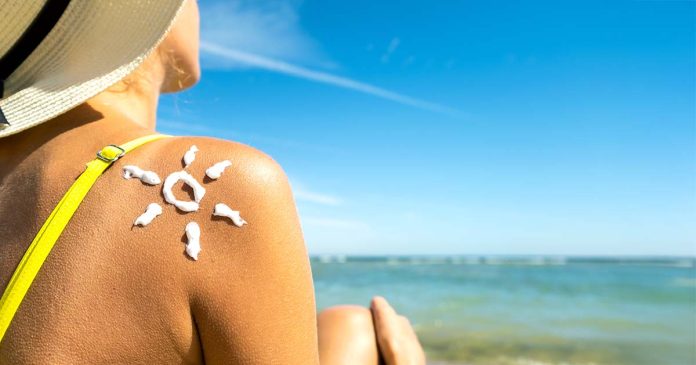 Essenciais de Verão para a Pele – Cuidados Uriage Pele com protetor solar em forma de sol no ombro de uma mulher na praia, ilustrando os essenciais de verão para a pele.