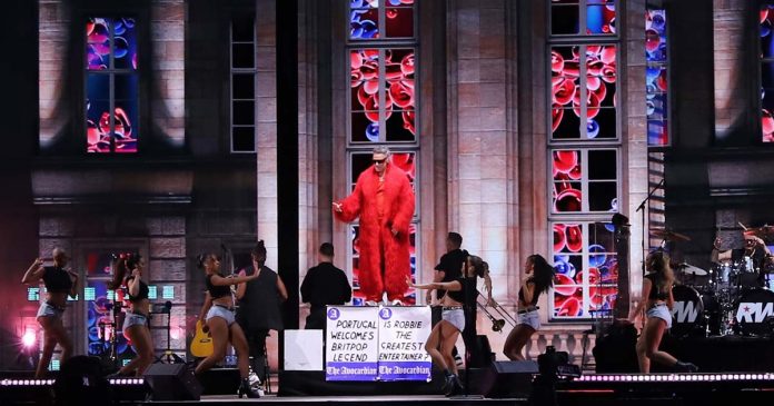 Robbie Williams de casaco vermelho comprido atua no palco principal do MEO Kalorama 2026 em Lisboa.