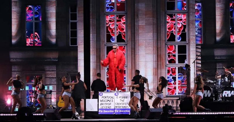 Robbie Williams de casaco vermelho comprido atua no palco principal do MEO Kalorama 2026 em Lisboa.