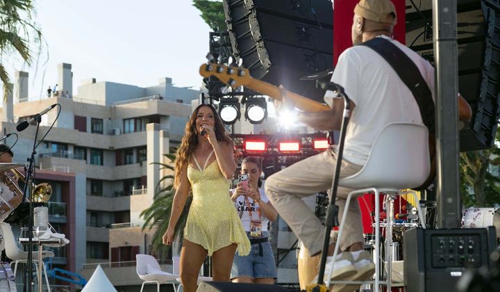 A artista Ivete Sangalo a cantar no centro do palco circular, com a banda ao redor, nos Jardins do Casino Estoril durante o projeto Ivete Clareou.