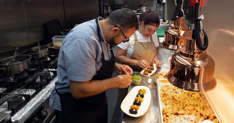 Equipa de cozinha do restaurante Vizinhos do Rei em Odivelas a empratar croquetes e entradas sob l&acirc;mpadas de aquecimento de cobre