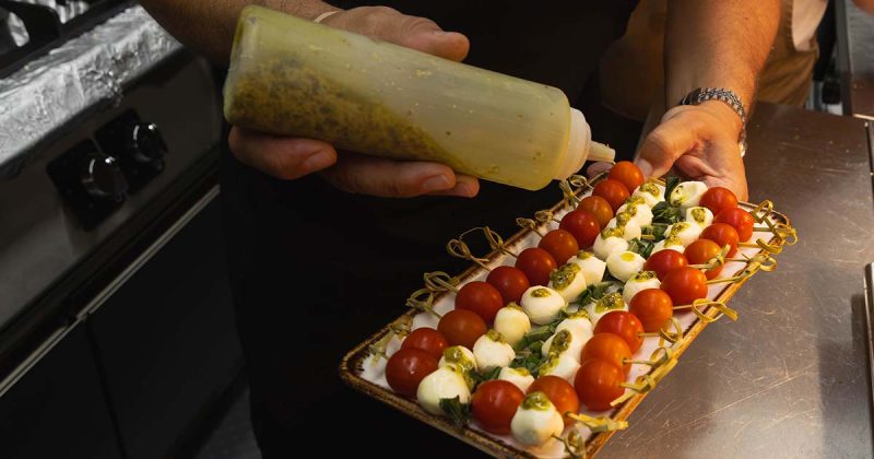 M&atilde;o do chef a aplicar molho pesto numa travessa com espetadas de tomate cherry e queijo mozzarella no restaurante Vizinhos do Rei em Odivelas