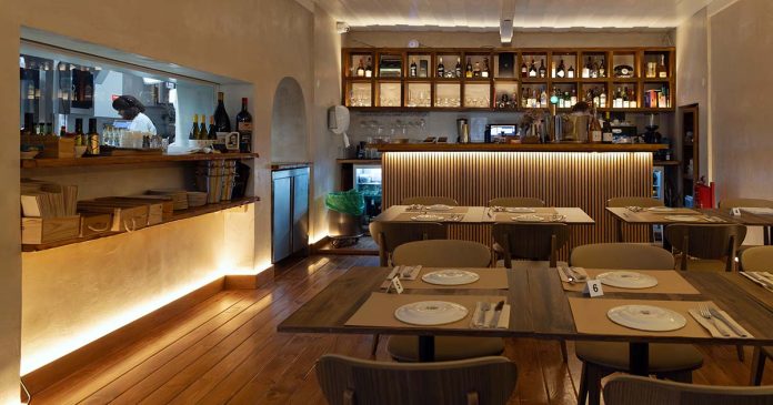 Sala principal do restaurante Vizinhos do Rei Interior da sala de refeições do restaurante Vizinhos do Rei em Odivelas com mesas dispostas e balcão iluminado ao fundo